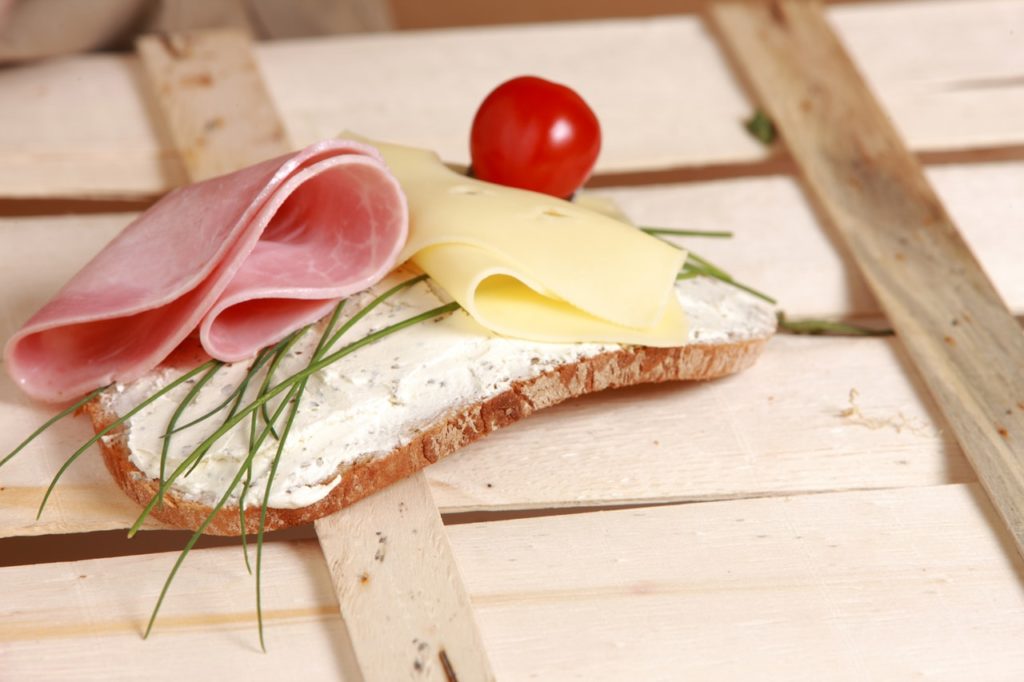 A slice of bread with ham, cheese, chives, and tomato