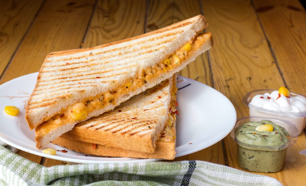 Two grilled sandwiches on a white plate next to two sauces