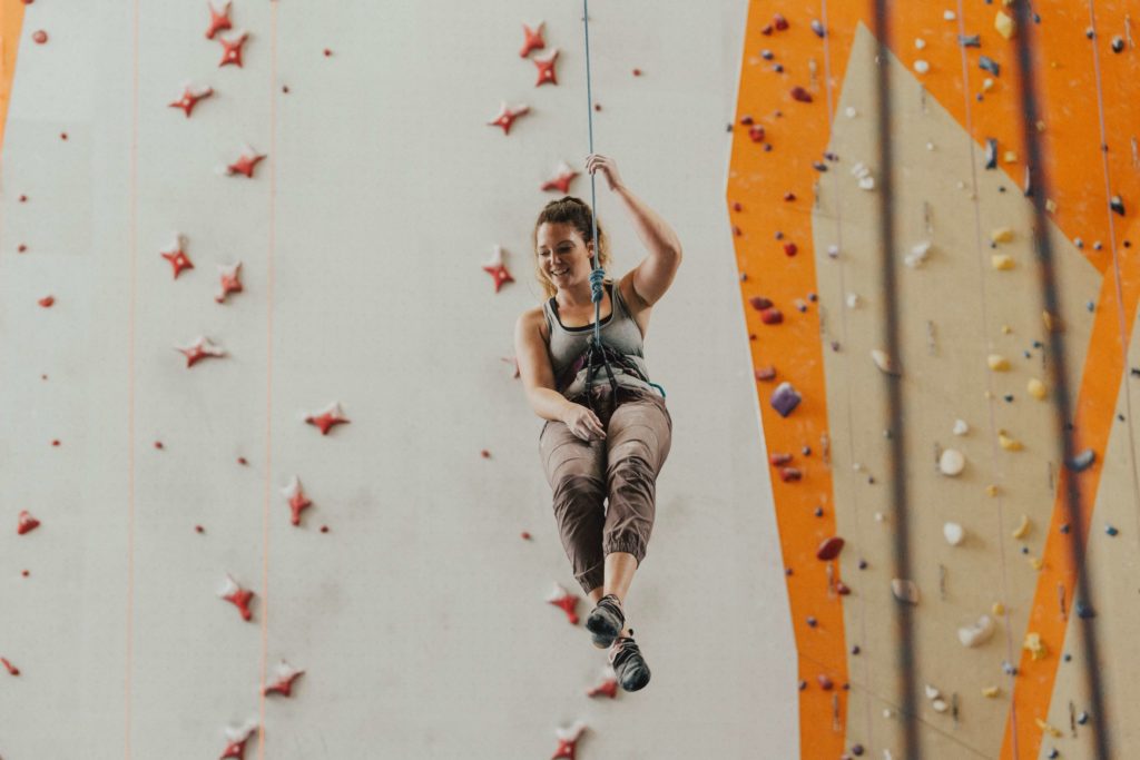 Girl attached to cables in front of a rock climbing wall
