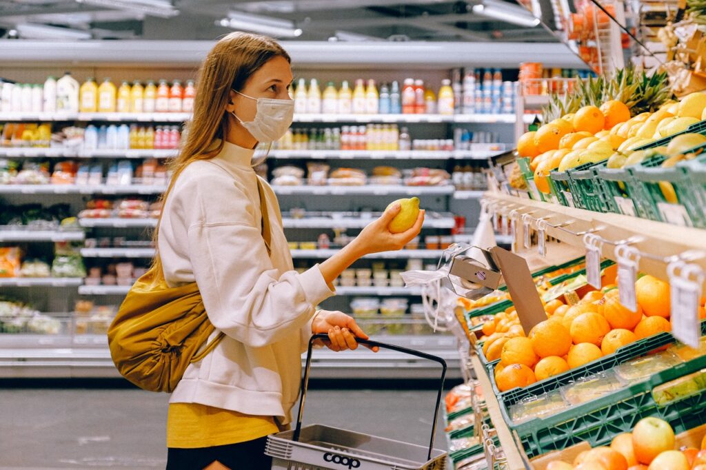 woman in yellow tshirt and beige jacket holding a fruit