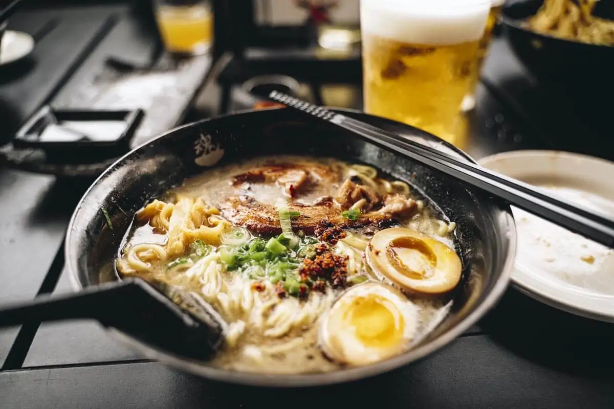 a bowl of ramen with chopsticks and a glass of beer