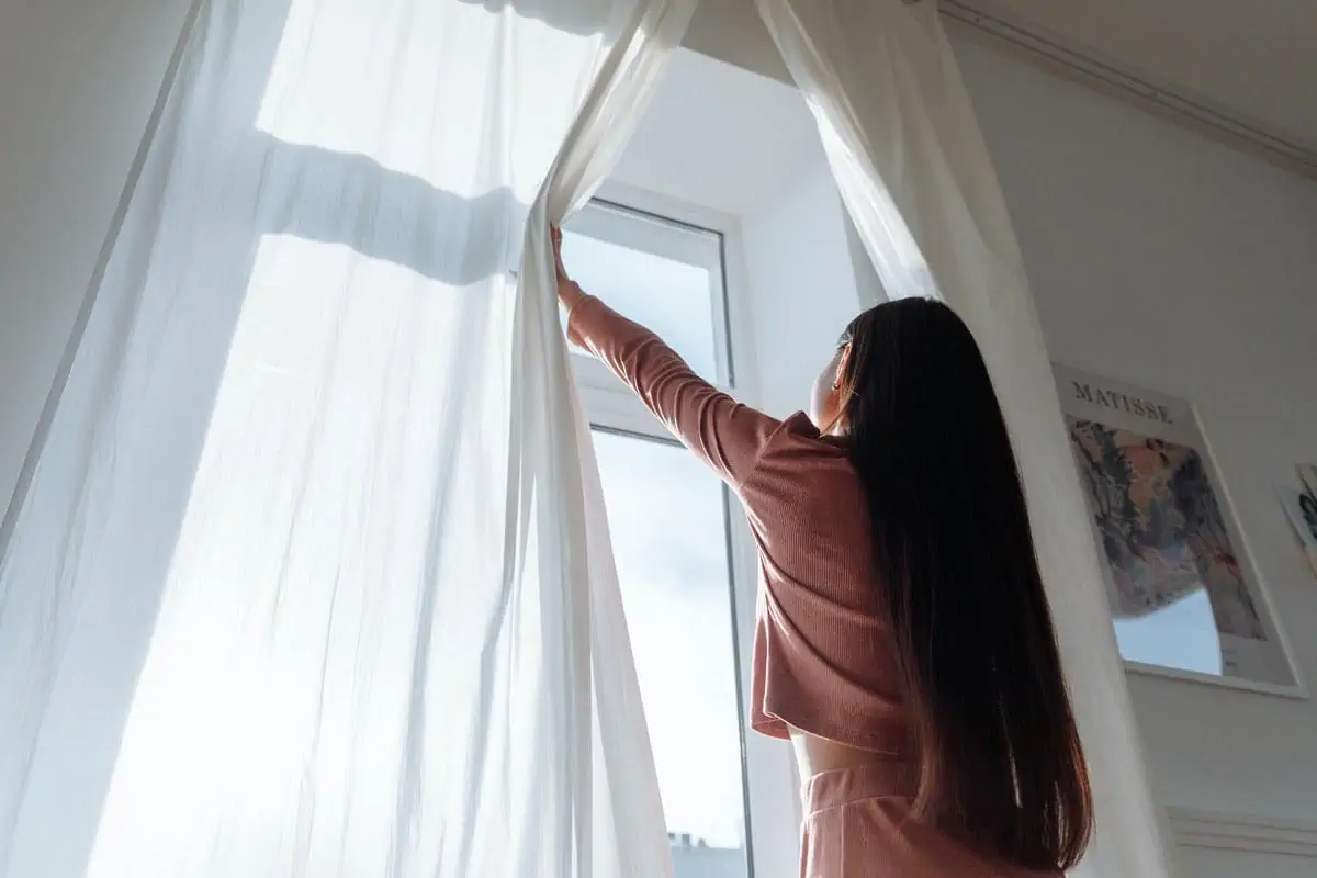 a woman opening a white curtain