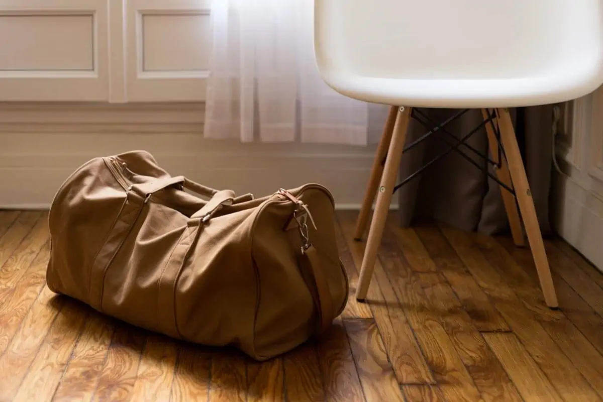 brown duffel bag beside white and brown wooden chair