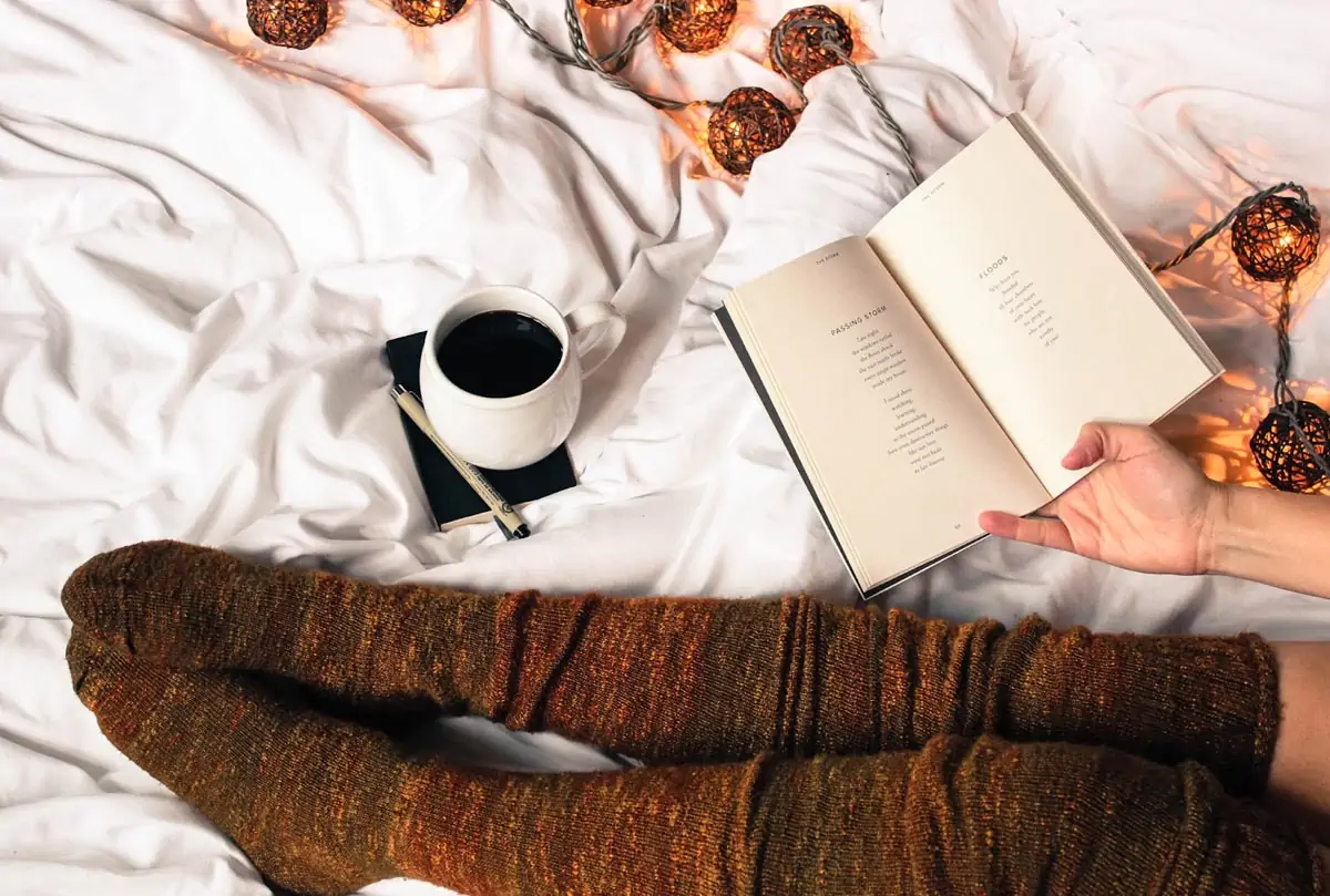 mug of black coffee beside persons feet wearing brown stockings