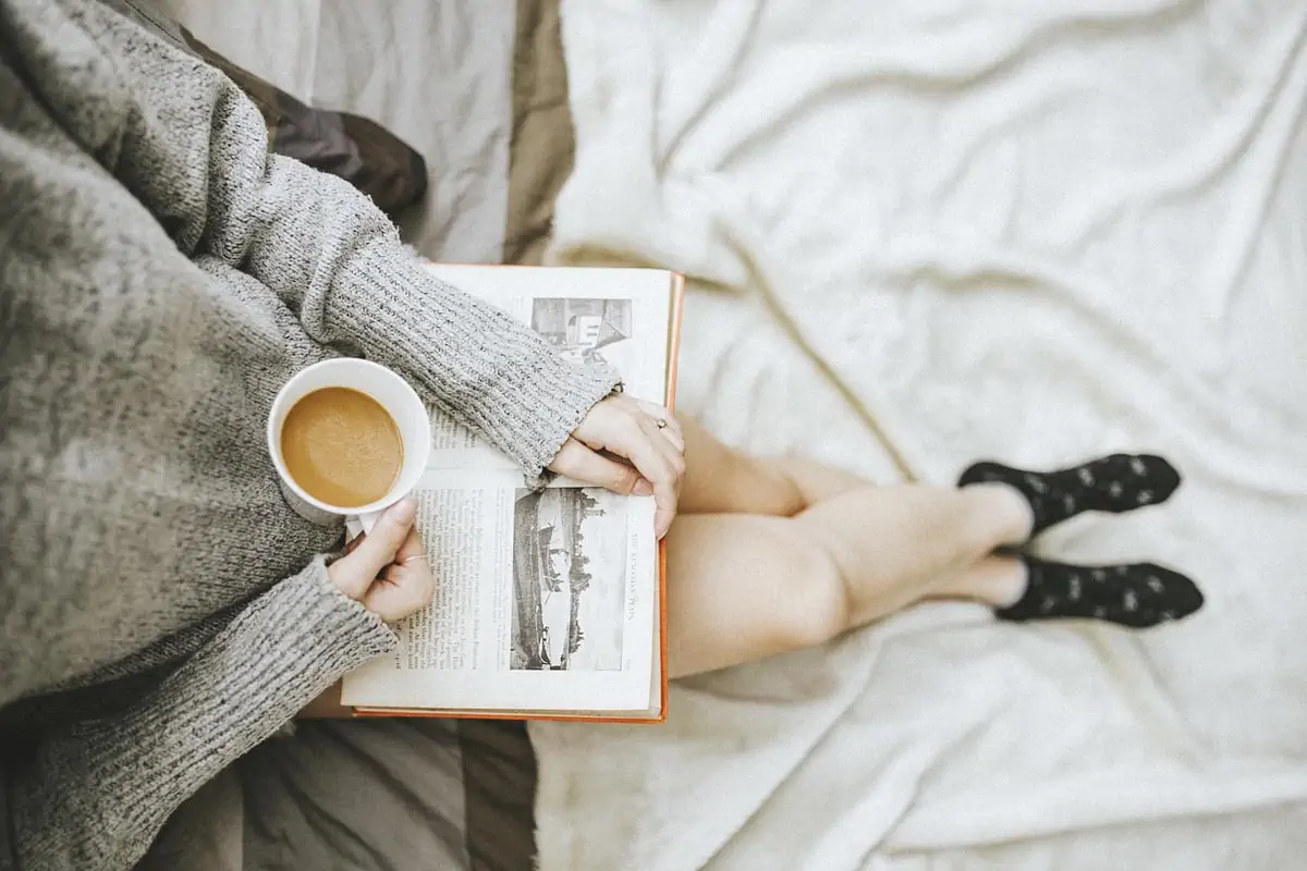 woman holding a cup of coffee at right hand and reading book on her lap