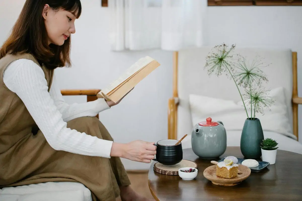 young woman reading book and having cup of tea