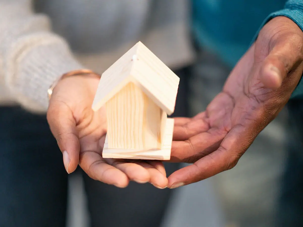 people-holding-miniature-wooden-house